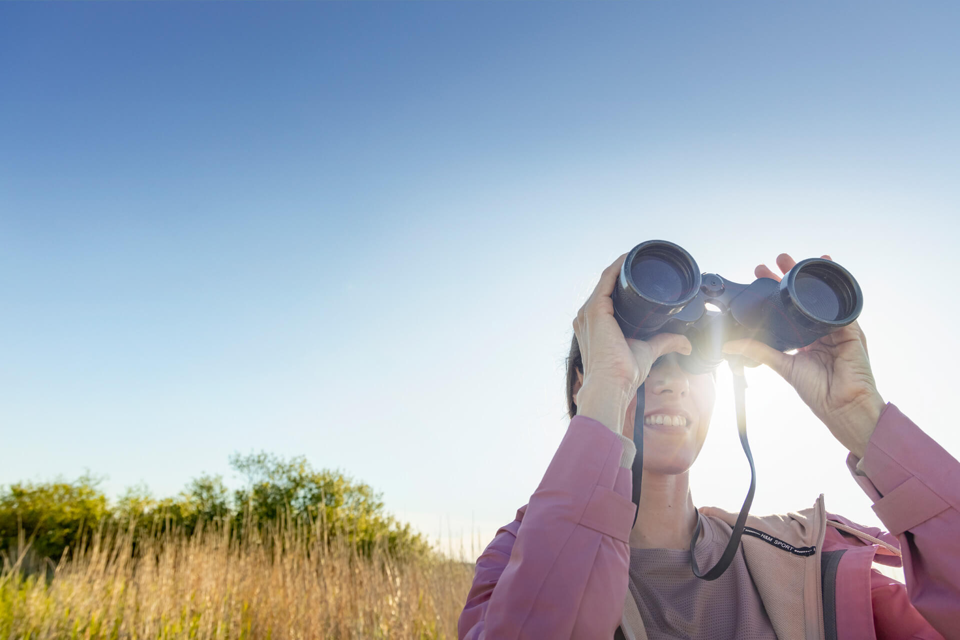 Woman looking through binoculars in a field and the sun is shining