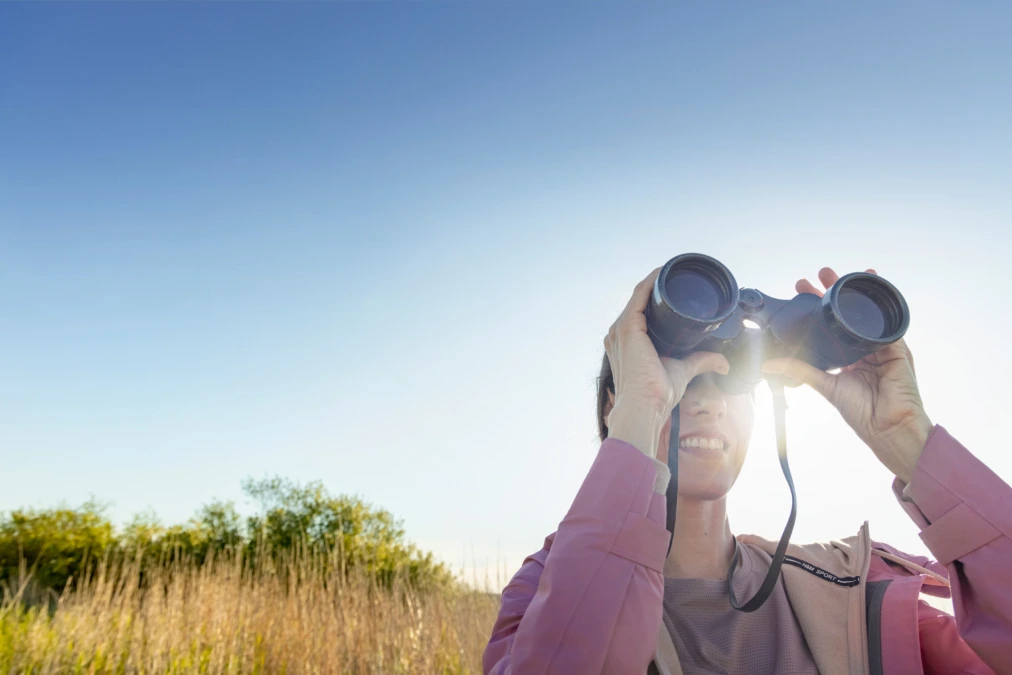 A woman is watching with binoculars.